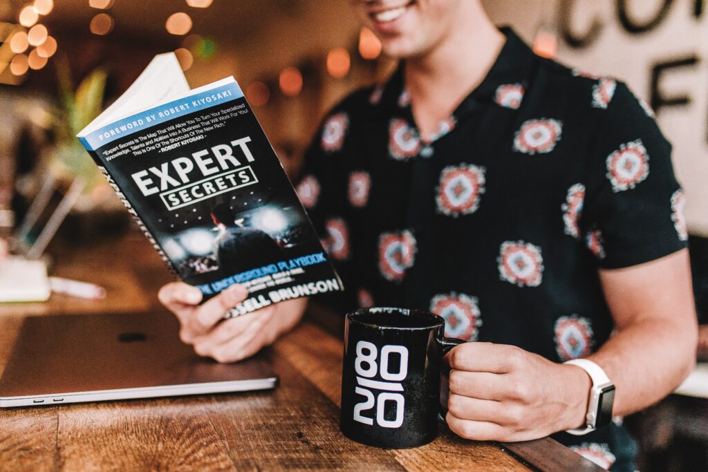 Man (presumably a Real Estate Agent) holding a book titled "Expert Secrets"