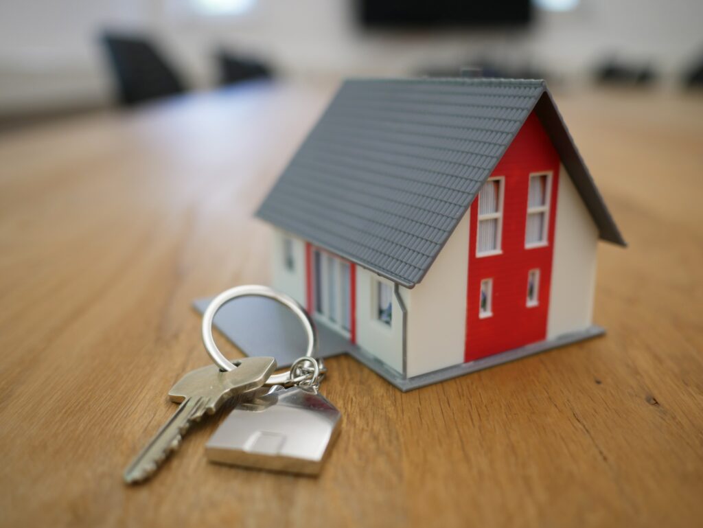 A silver key next to a miniature house. Caption: Escrow is your trusty third-party that holds assets in behalf all parties until obligations have been met. 